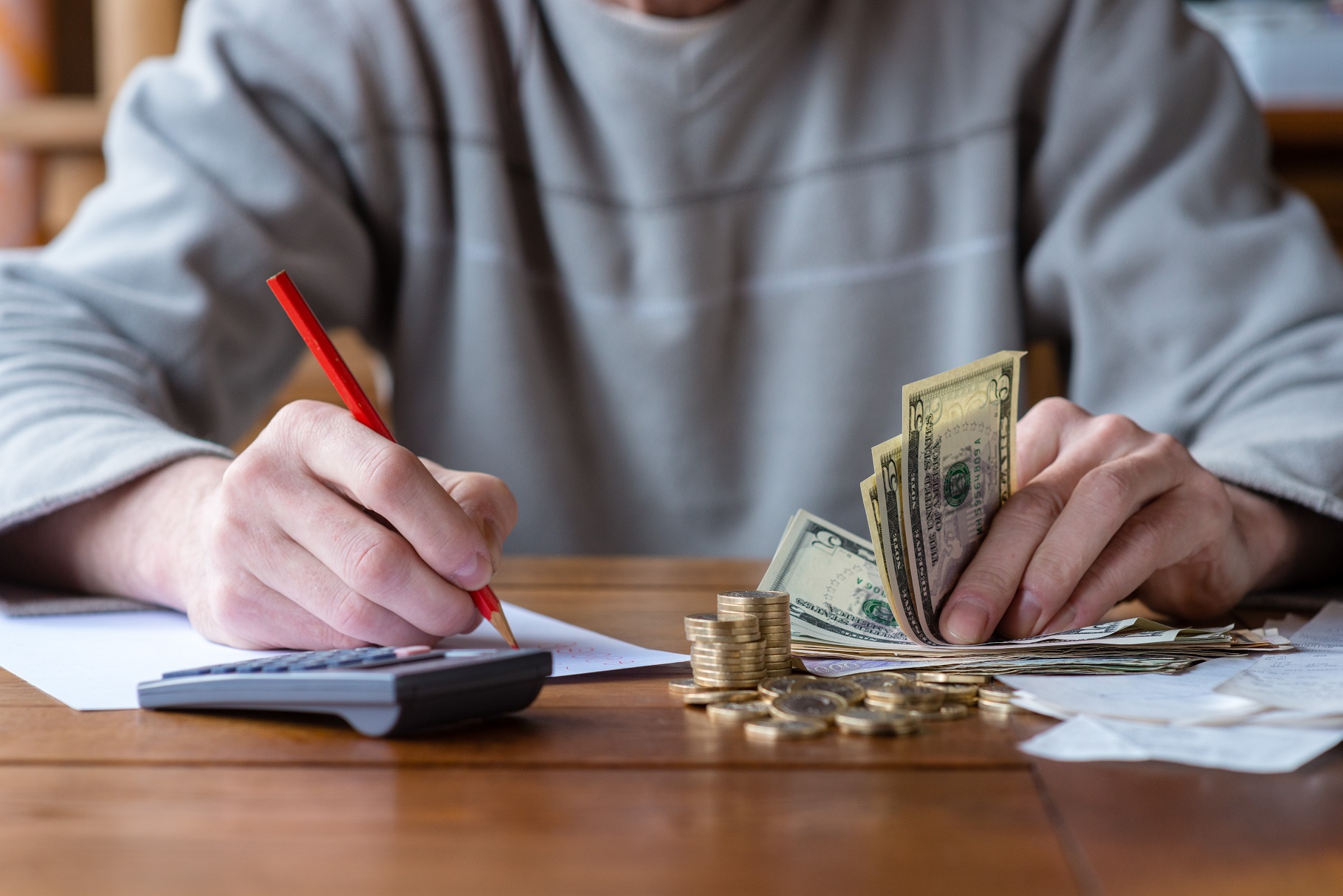 Close up man with calculator counting, making notes at home, hand is writes in a notebook. Stacked coins arranged at desk. Savings finances concept.